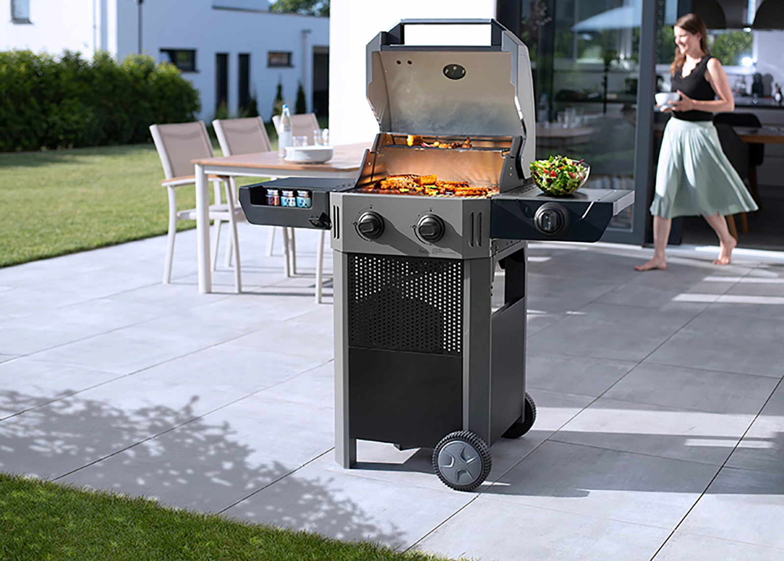 E-Grill auf einer Terrasse mit einer Frau im Hintergrund
