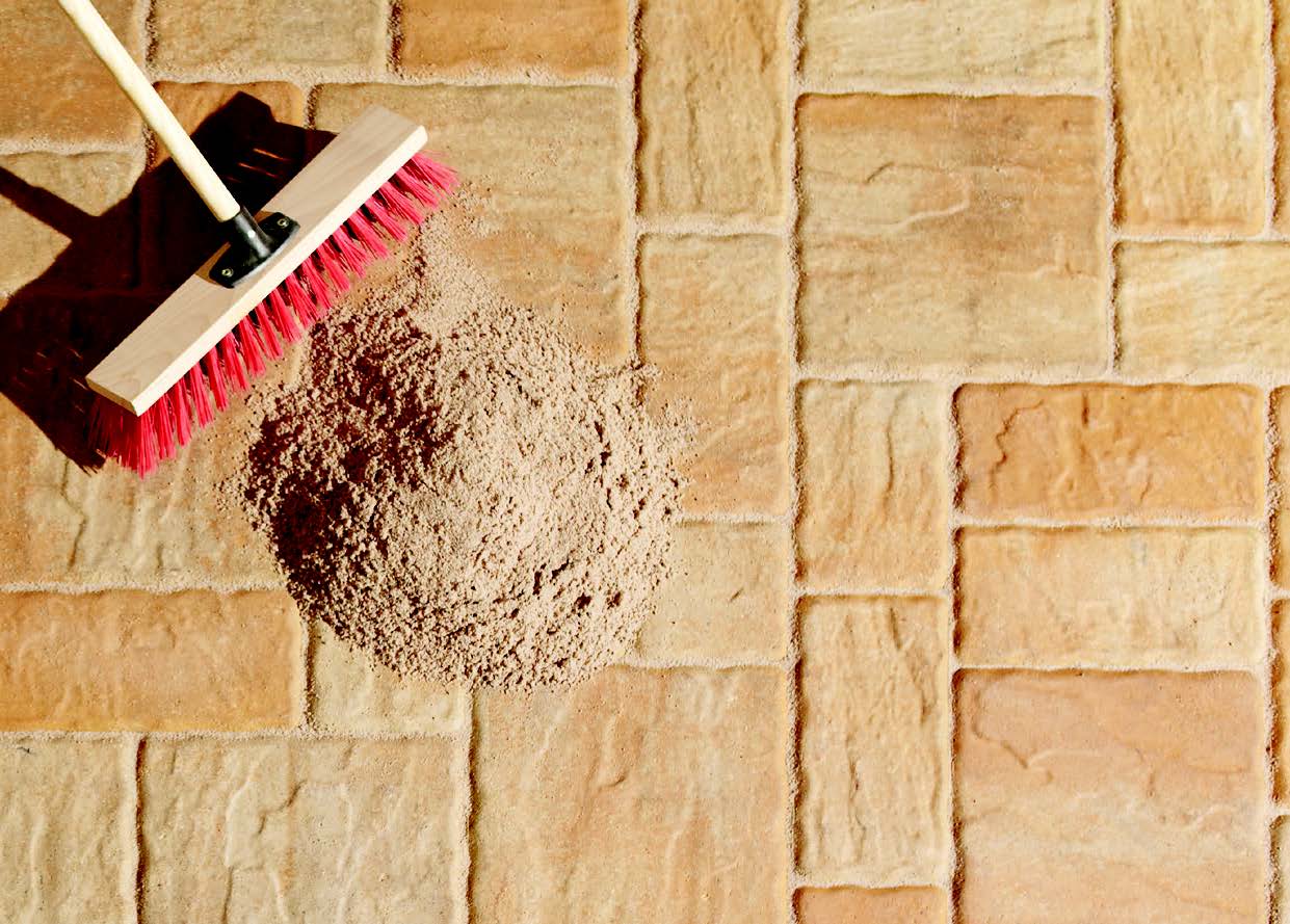 Sand wird mit einem Besen in die Fugen verteilt